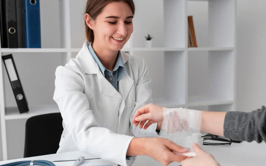 Course banner for "Cuts, Wounds and Blue Plasters: Handling Food Safely with an Injury," showing a smiling female healthcare professional or occupational nurse dressing a patient's arm injury with a white bandage in a medical office.