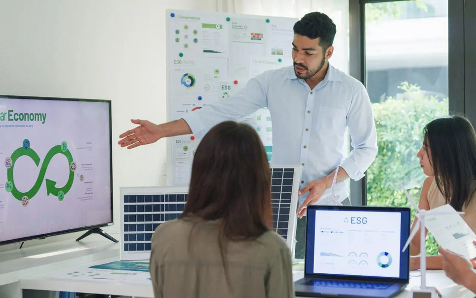A man standing and presenting a circular economy diagram on a screen and charts to colleagues during an ESG strategy meeting in an office