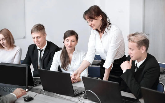 A female instructor pointing at a laptop screen while assisting a professional team during an AI governance and data protection training session in an office