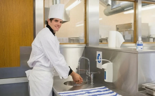 Educational guide banner for "How to Wash Your Hands Properly in a Food Business (Step by Step)," depicting a kitchen worker demonstrating proper handwashing techniques and personal hygiene compliance in a food service setting.