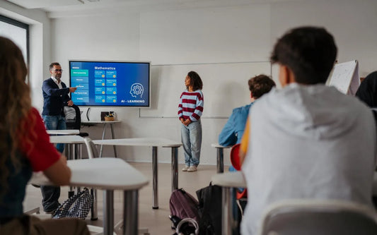 A teacher pointing at a mathematics and AI learning screen during a classroom session while a student stands in front of seated classmates