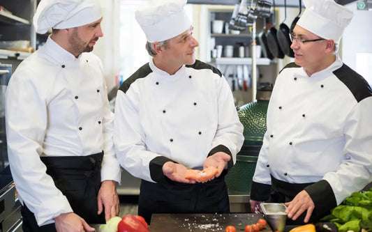 Three chefs discussing food handling procedures in a professional commercial kitchen.