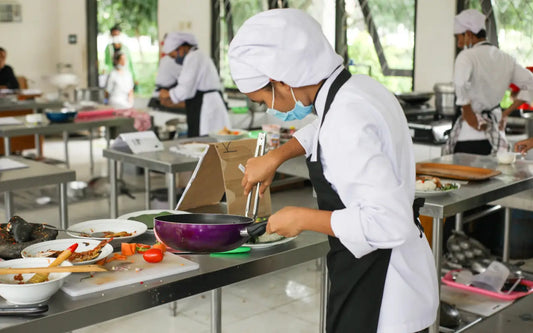 Chef preparing food at a workstation in a busy commercial kitchen with other kitchen staff.