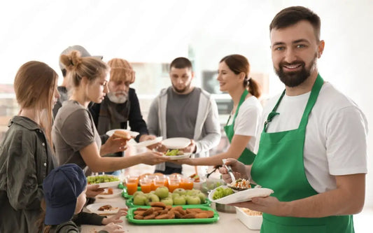 Food service volunteers in green aprons distributing prepared meals at a community charity event.