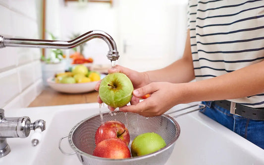 Person washing fresh red and green apples under running water in a kitchen sink.